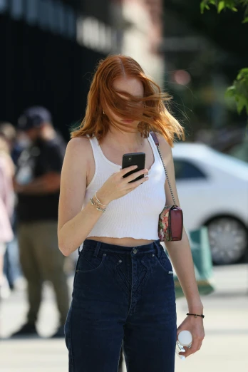 a woman walking down the street looking at her cell phone, trending on pexels, renaissance, sadie sink, bare midriff, white top, christina hendricks