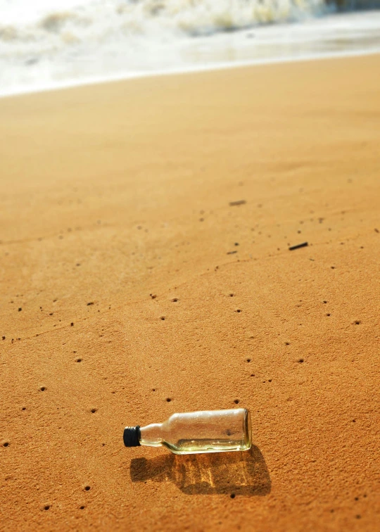 a bottle sitting on top of a sandy beach, on the ocean, brown water