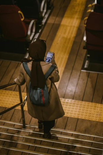 a woman walking down a set of stairs holding a cell phone, by Niko Henrichon, trending on unsplash, happening, wearing a brown cape, in a cinema, photograph from above, trending in japan