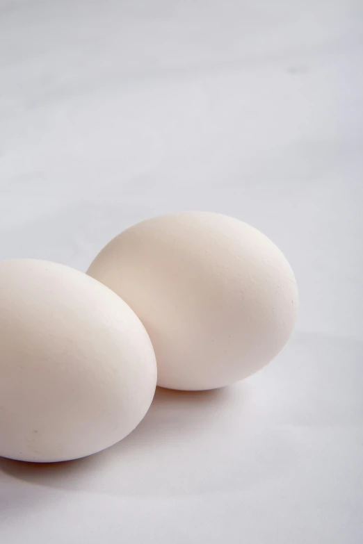 two eggs sitting next to each other on a table, white backdrop, up-close, recipe, shaven