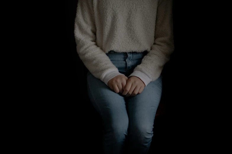 a woman sitting on a chair in the dark, white sweater, holding hands, background image, underexposed