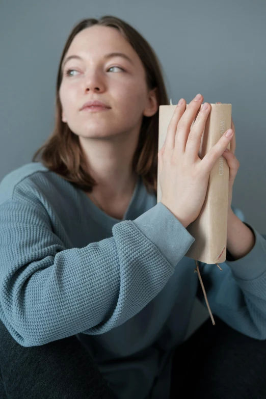 a woman sitting on the floor holding a book, inspired by Sarah Lucas, renaissance, hands shielding face, scaled arm, sustainable materials, prayer