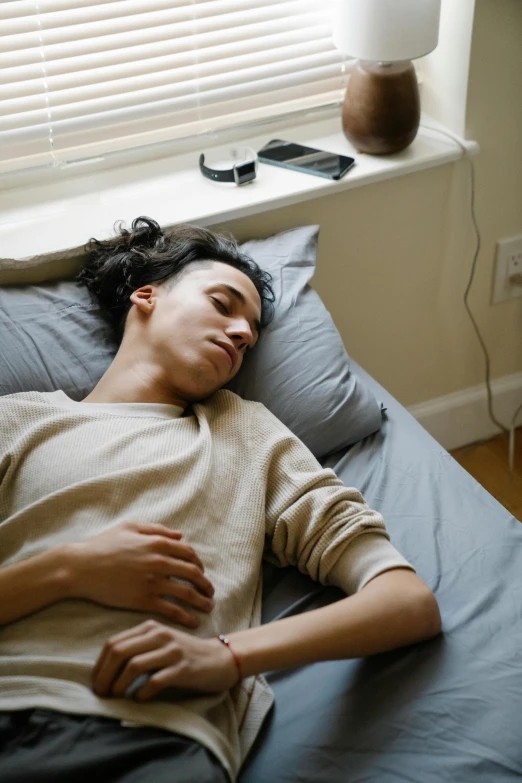 a man laying on top of a bed next to a window, trending on pexels, renaissance, androgynous person, 1 6 years old, asleep, high angle