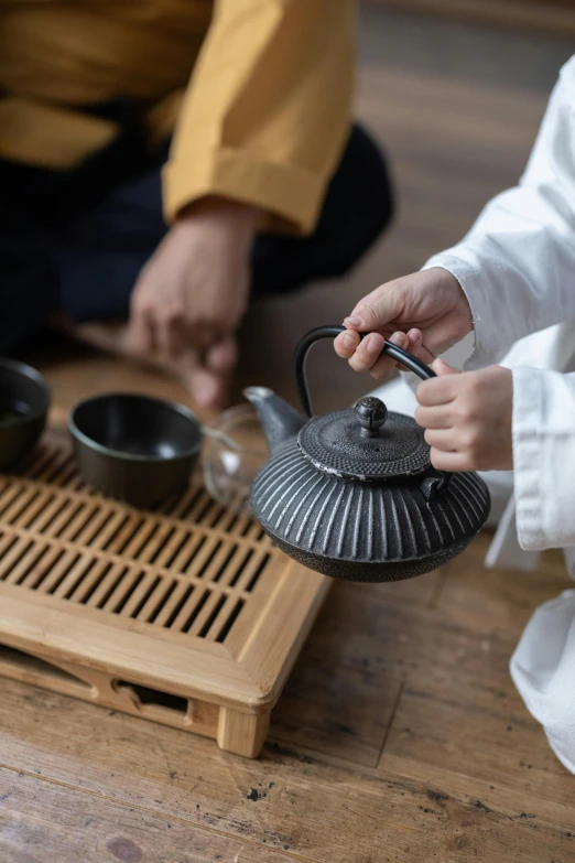 a couple of people that are sitting on the floor, inspired by Sesshū Tōyō, trending on unsplash, mingei, teapot, hand on table, square, high-quality photo