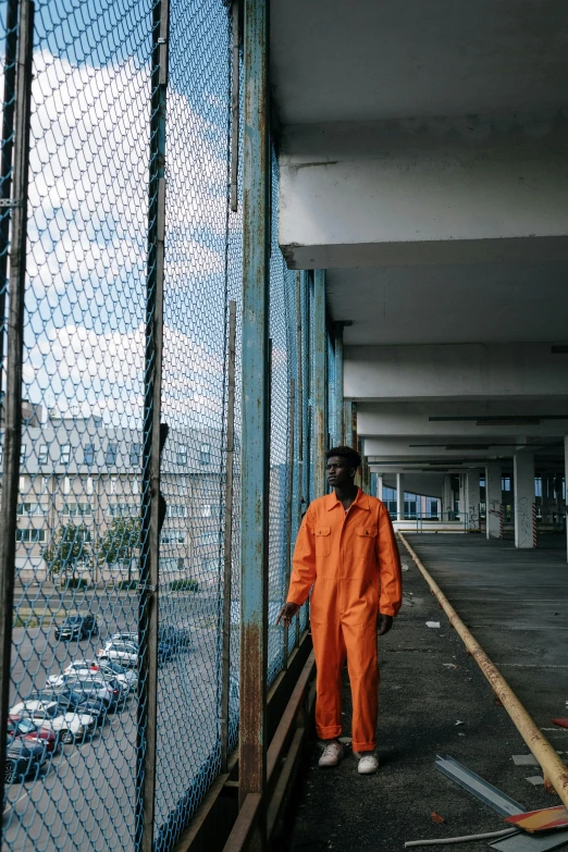 a man in an orange jumpsuit walking down a walkway, an album cover, pexels contest winner, detention centre, dark skinned, fences, vsco