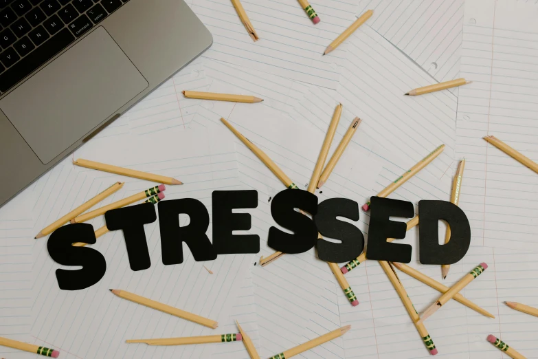 a laptop computer sitting on top of a desk next to a pile of pencils, trending on pexels, process art, stressed out, handwriting title on the left, stress, crossed arms