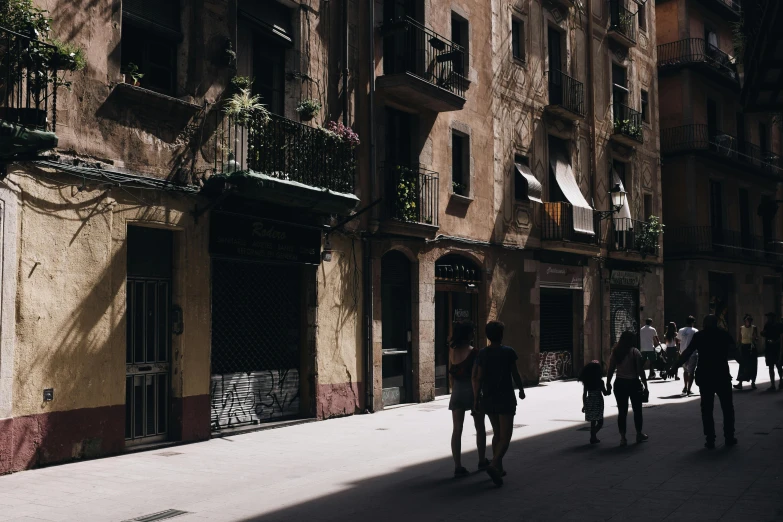 a group of people walking down a street next to tall buildings, a photo, pexels contest winner, gothic quarter, summer light, gif, ignant