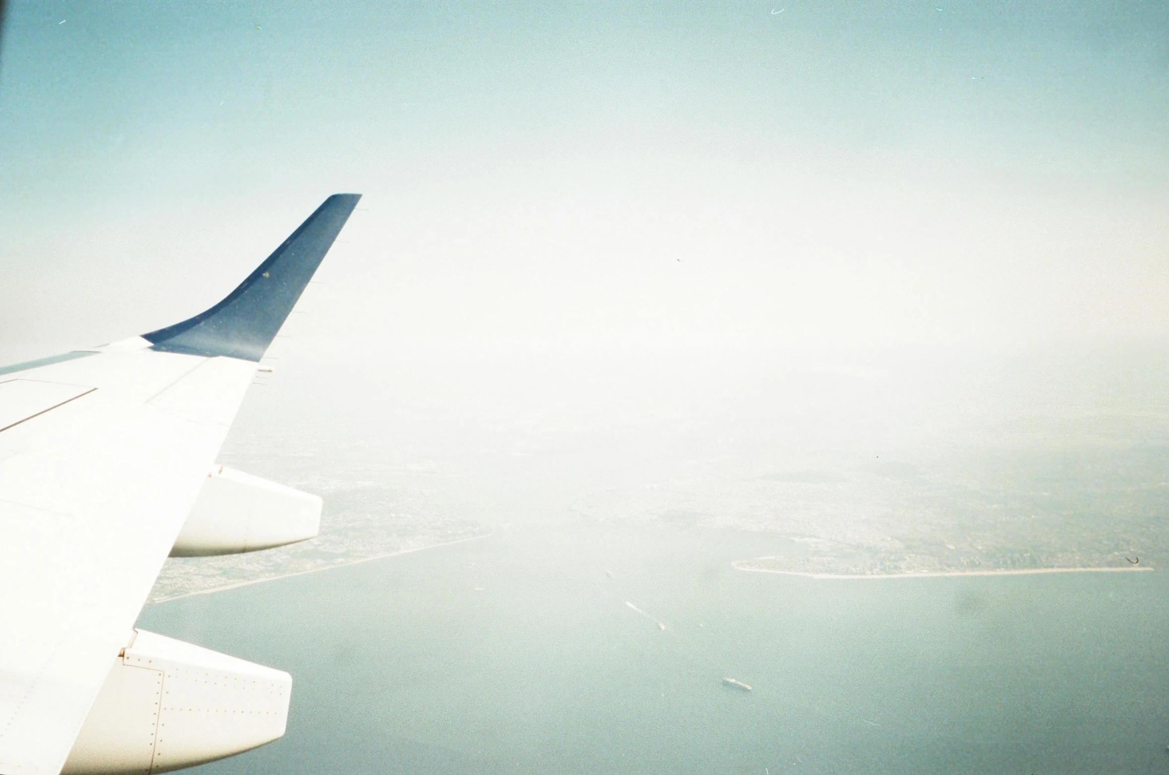 the wing of an airplane flying over a body of water, a picture, unsplash, minimalism, new york city, dreamy hazy, portra 8 0 0 ”, airplanes