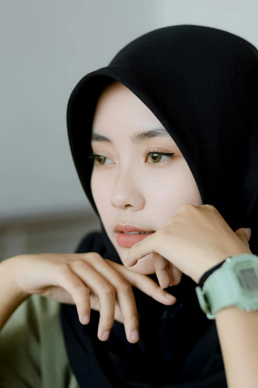 a woman wearing a black hijab sitting on a couch, by Basuki Abdullah, trending on pexels, realism, wearing a watch, light green tone beautiful face, thoughtful ), square