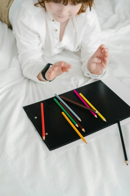 a little girl laying on a bed with colored pencils, trending on pexels, visual art, hotel room, black, flat lay, hand gestures