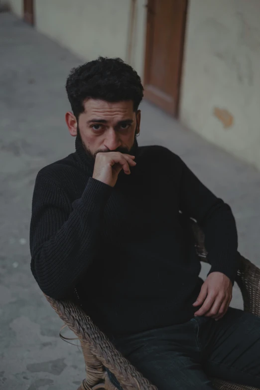 a man sitting on top of a wicker chair, a character portrait, by Ismail Acar, pexels contest winner, black turtle neck shirt, thoughtful expression, middle eastern, ( ( theatrical ) )