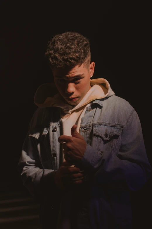 a man in a denim jacket standing in the dark, an album cover, by Robbie Trevino, trending on pexels, realism, teen boy, bad bunny, julian ope, concert