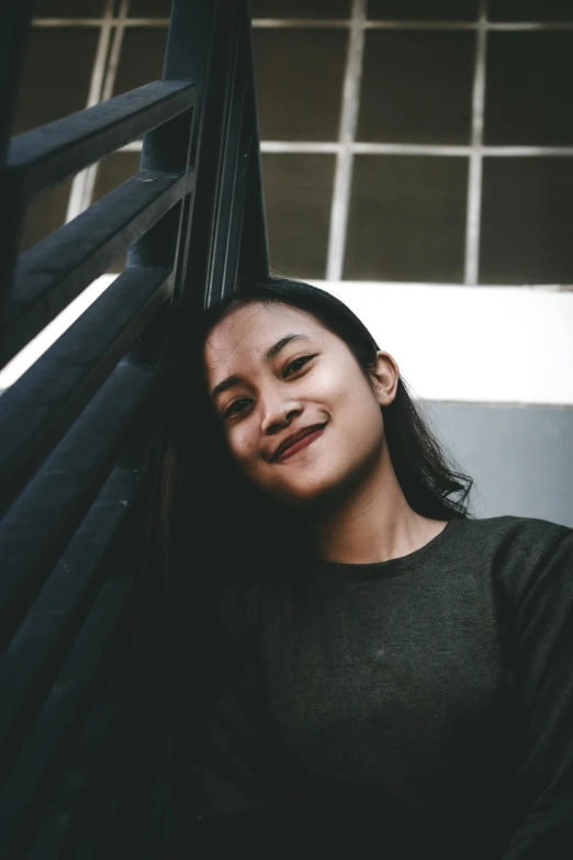 a woman leaning against a railing with her eyes closed, pexels contest winner, happening, wearing jeans and a black hoodie, south east asian with round face, happy girl, portrait of ((mischievous))