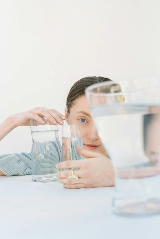 a woman sitting at a table with a glass of water, an album cover, by Nicolette Macnamara, trending on pexels, half face in the water, on a pale background, made of water, high quality picture