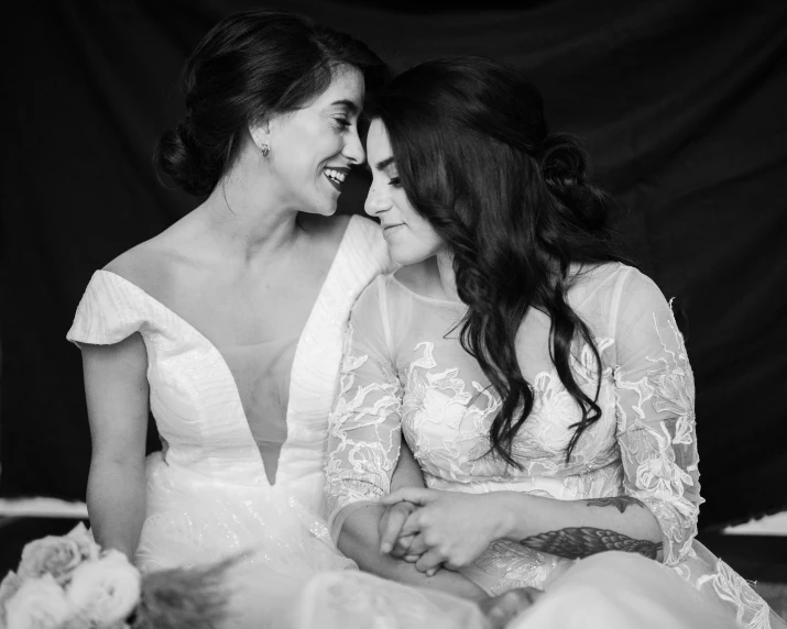 a couple of women sitting next to each other, a black and white photo, by Emma Andijewska, pexels, art nouveau, bride, brunettes, lesbian embrace, happy