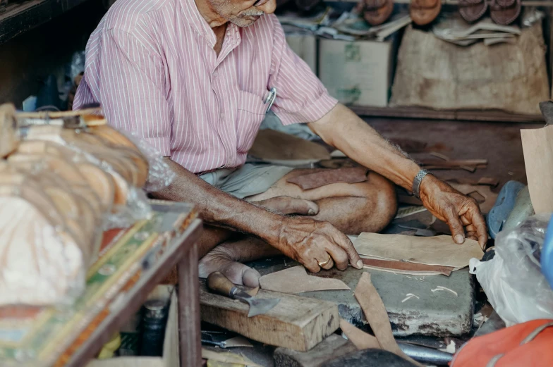 a man that is sitting down making something, by William Berra, pexels contest winner, leather straps, avatar image, batik, artificial limbs