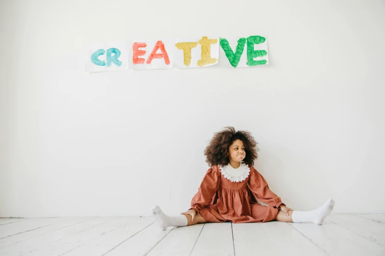 a little girl sitting on the floor in front of a sign that says creative, a child's drawing, pexels contest winner, african american elegant girl, woman in streetwear, costume, wall painting