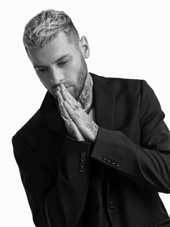 a black and white photo of a man in a suit, an album cover, trending on pexels, tattooed man, praying, blonde man, liam