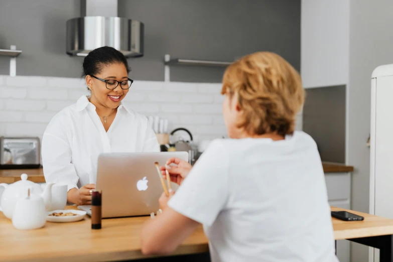 a woman sitting at a kitchen table with a laptop, pexels contest winner, doctors office, smiling at each other, wolfy nail, manuka