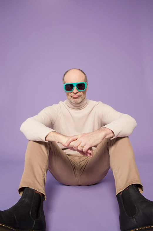 a man sitting on top of a bean bag, inspired by Leo Leuppi, cool sunglasses, bald lines, wearing turtleneck, green and purple studio lighting