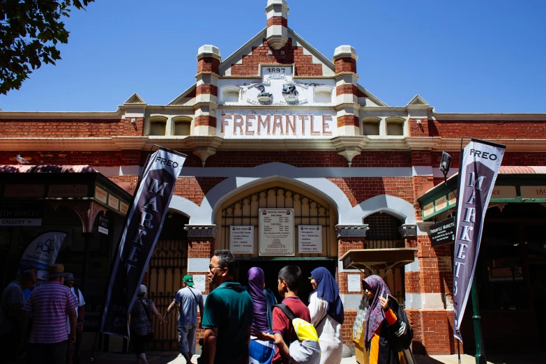 a group of people standing in front of a building, train station in summer, dreamworld, archway, heatwave