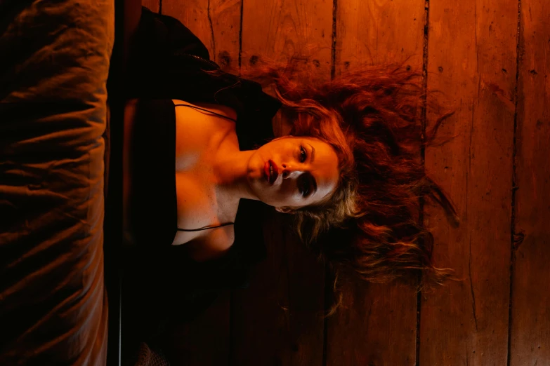a woman laying on top of a bed next to a wooden wall, a portrait, inspired by Elsa Bleda, pexels contest winner, renaissance, beautiful scary female vampire, wild ginger hair, saturday night in a saloon, looking down on the camera