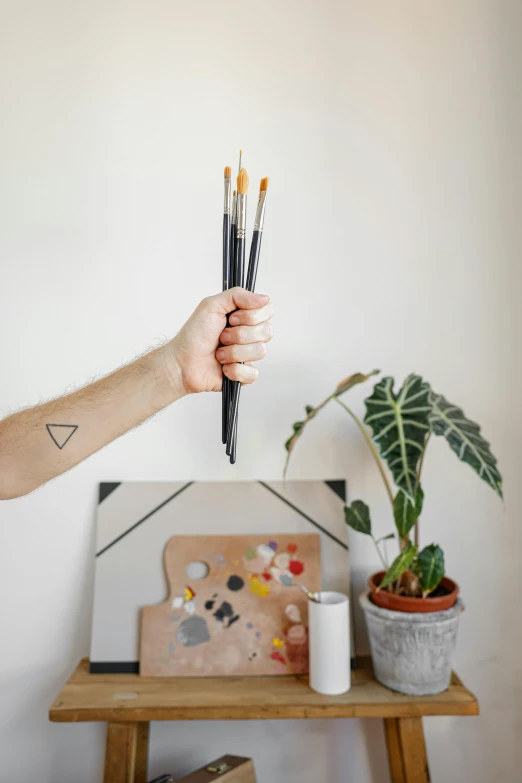 a man holding a paintbrush next to a potted plant, a minimalist painting, trending on pexels, temporary tattoo, holding paintbrushes, medium: black pencil, studio product shot