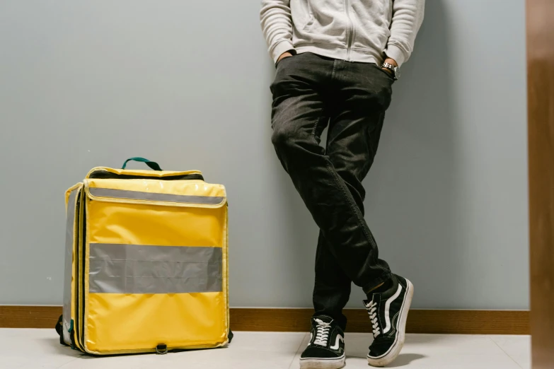 a man leaning against a wall next to a suitcase, trending on pexels, yellow and black trim, healthcare worker, reflective material, product design shot