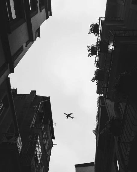 a black and white photo of an airplane in the sky, by Adam Rex, pexels contest winner, raising between the buildings, istanbul, alleys, high quality image”