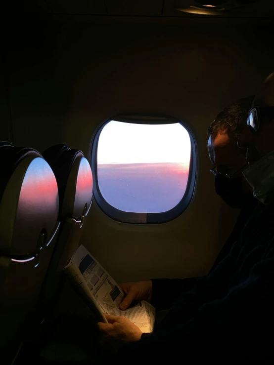 a man sitting in an airplane reading a book, a picture, by Carey Morris, pexels contest winner, happening, vaporwave sunset, eyes projected onto visor, profile image, the sky is a faint misty red hue