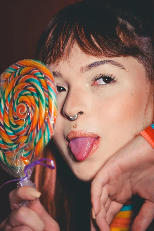 a woman holding a lollipop in front of her face, inspired by Elsa Bleda, trending on pexels, pop art, hailee steinfeld, straight bangs, spiral, lesbians