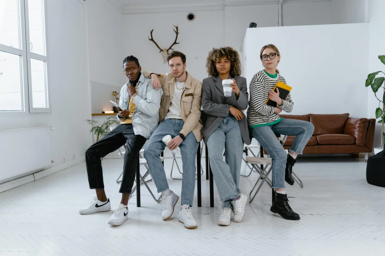 a group of people sitting on chairs in a room, trending on pexels, androgynous person, blue jeans and grey sneakers, nerds, brown clothes