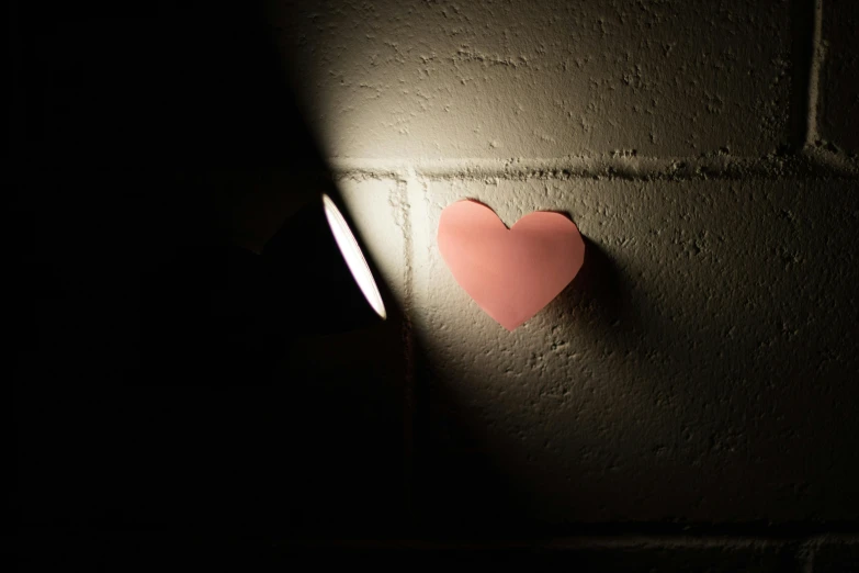 a heart shaped piece of paper on a wall, inspired by Robert Mapplethorpe, unsplash, flashlight on, pink, medium angle, indoor picture