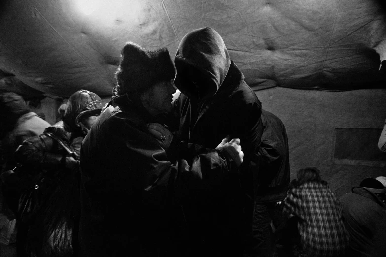 a black and white photo of a group of people, by Anato Finnstark, unsplash, symbolism, tickle fight in the death tent, cold freezing nights, two men hugging, hooded figures