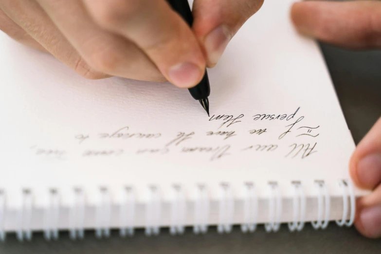 a person writing on a piece of paper with a pen, unsplash, letterism, fan favorite, calligraphic poetry, low quality photo, thumbnail