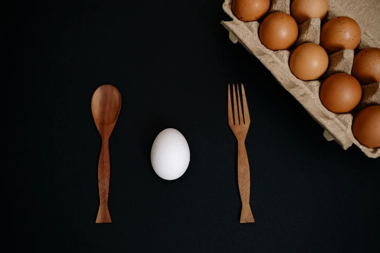 an egg, fork and spoon next to a carton of eggs, a still life, unsplash, a wooden, in front of a black background, fork fork fork, miniature product photo