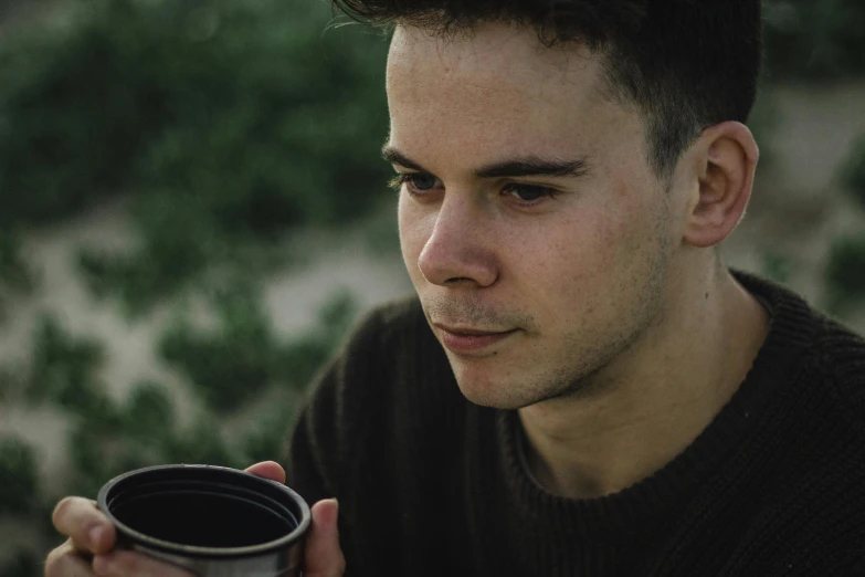 a close up of a person holding a cup, by Adam Marczyński, young male, concentrated, julian ope, outdoor photo