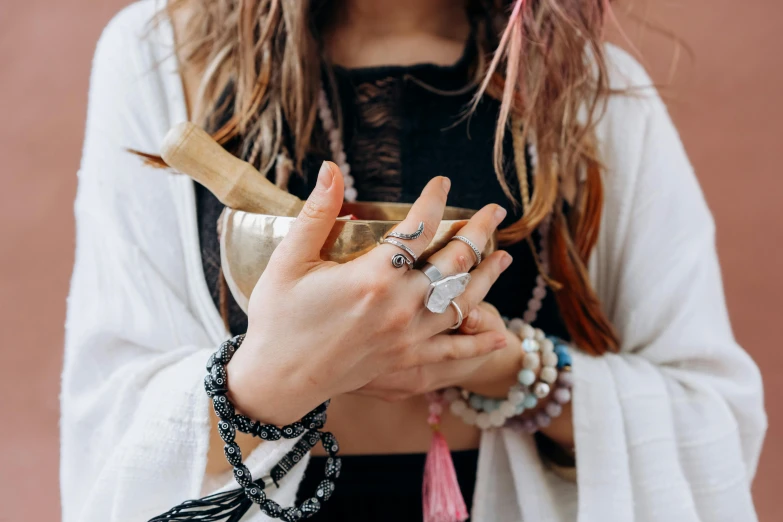 a woman holding a wooden spoon in her hands, an album cover, by Julia Pishtar, trending on pexels, chakras, armillary rings jewelry, holding a bell, bracelets