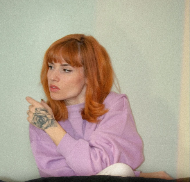 a woman sitting on top of a bed holding a remote, a colorized photo, inspired by Elsa Bleda, trending on pexels, hyperrealism, orange hair, wearing a purple sweatsuit, bangs, calmly conversing 8k