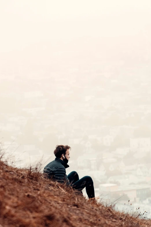 a man sitting on top of a hill talking on a cell phone, pexels, city fog, scruffy man, bleak color, without text