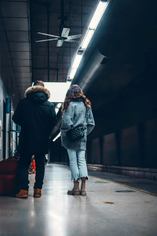 a couple of people standing next to each other with luggage, by Niko Henrichon, pexels contest winner, tunnel, lone girl waiting for the train, wearing jeans and a black hoodie, exiting store