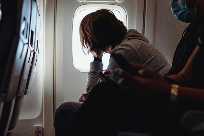 a woman sitting in an airplane looking out the window, pexels contest winner, happening, sad men, hunched over, teenage girl, air is being pushed around him