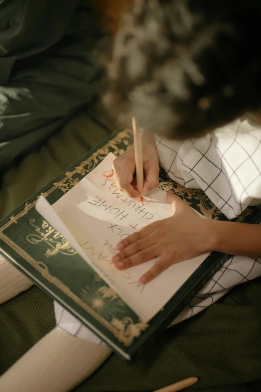 a person sitting on a bed writing on a piece of paper, spell book, green and brown clothes, thumbnail, islamic