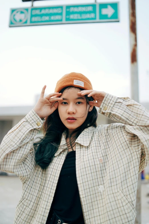 a woman standing in front of a street sign, inspired by Kim Jeong-hui, trending on pexels, wearing a beanie, wearing a flannel shirt, profile image, orange jacket