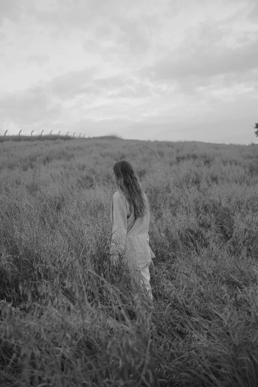 a woman standing in a field of tall grass, a black and white photo, still from a music video, walking away, asher duran, waist long hair