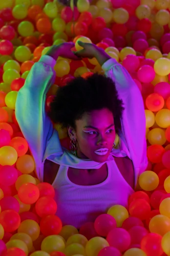 a woman laying on top of a ball pit, an album cover, colored gel lighting, black young woman, hanging out with orbs, video still