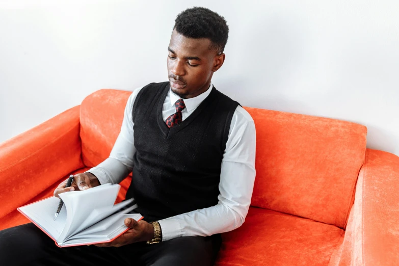 a man sitting on a couch holding a piece of paper, by Carey Morris, pexels contest winner, red tie, ( ( dark skin ) ), studious, academic clothing