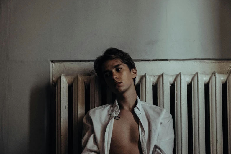 a shirtless man sitting in front of a radiator, an album cover, by Emma Andijewska, pexels contest winner, bauhaus, delicate androgynous prince, young teen, white clothes, portrait soft low light