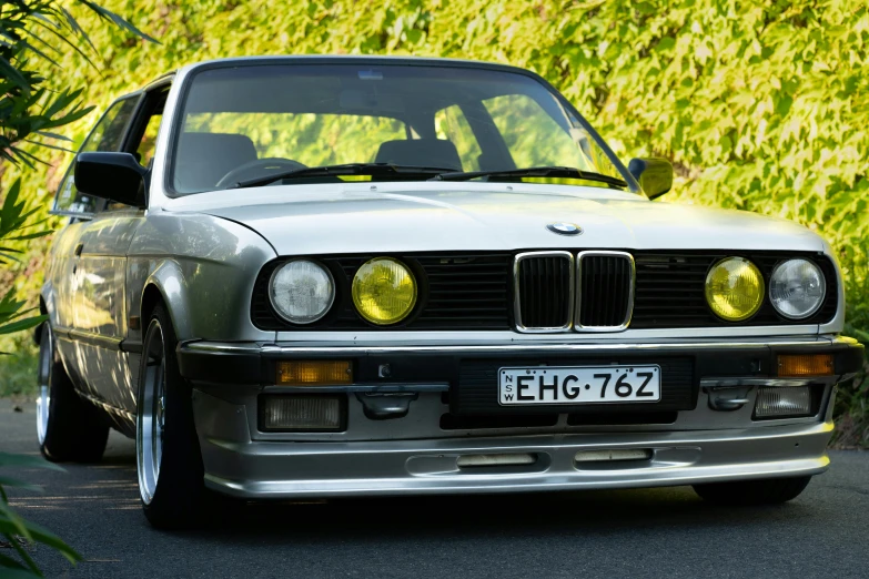 a silver car parked on the side of the road, inspired by Harry Haenigsen, unsplash, renaissance, bmw e 3 0, with a bright yellow aureola, “ iron bark, front lit