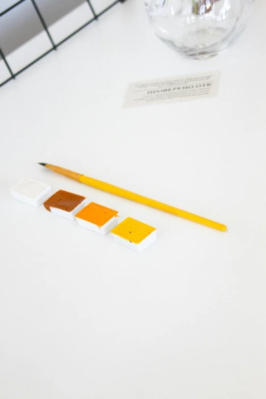 a couple of pencils sitting on top of a table, yellow and orange color scheme, on white paper, cubes on table, pigment